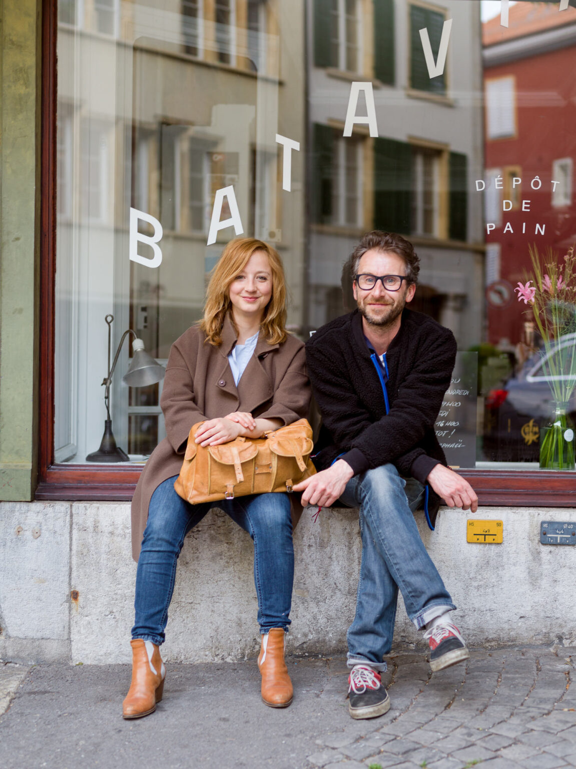 Die beiden Besitzer der Epicerie Batavia sitzen vor ihrem Laden und lächeln in die Kamera für die Firmenfotos.