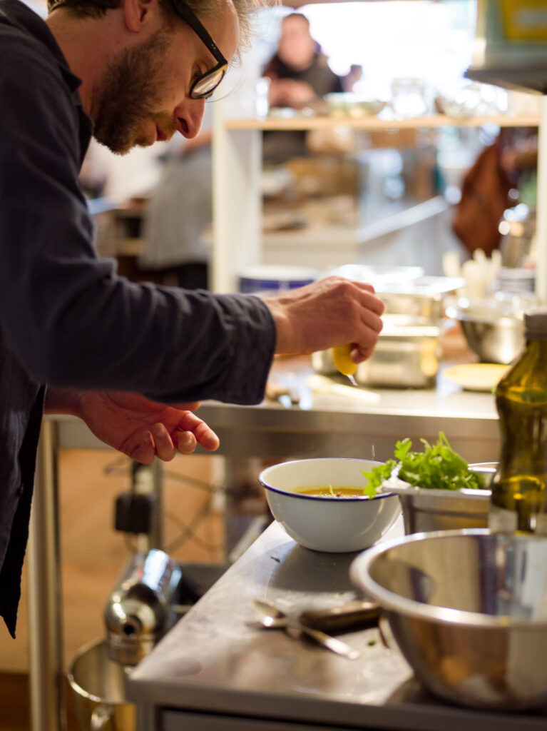 Reportage Bild von Raphaël, der Zitronensaft in eine Suppe presst. Eine Momentaufnahmen der Reportage über die Epicerie Batavia.