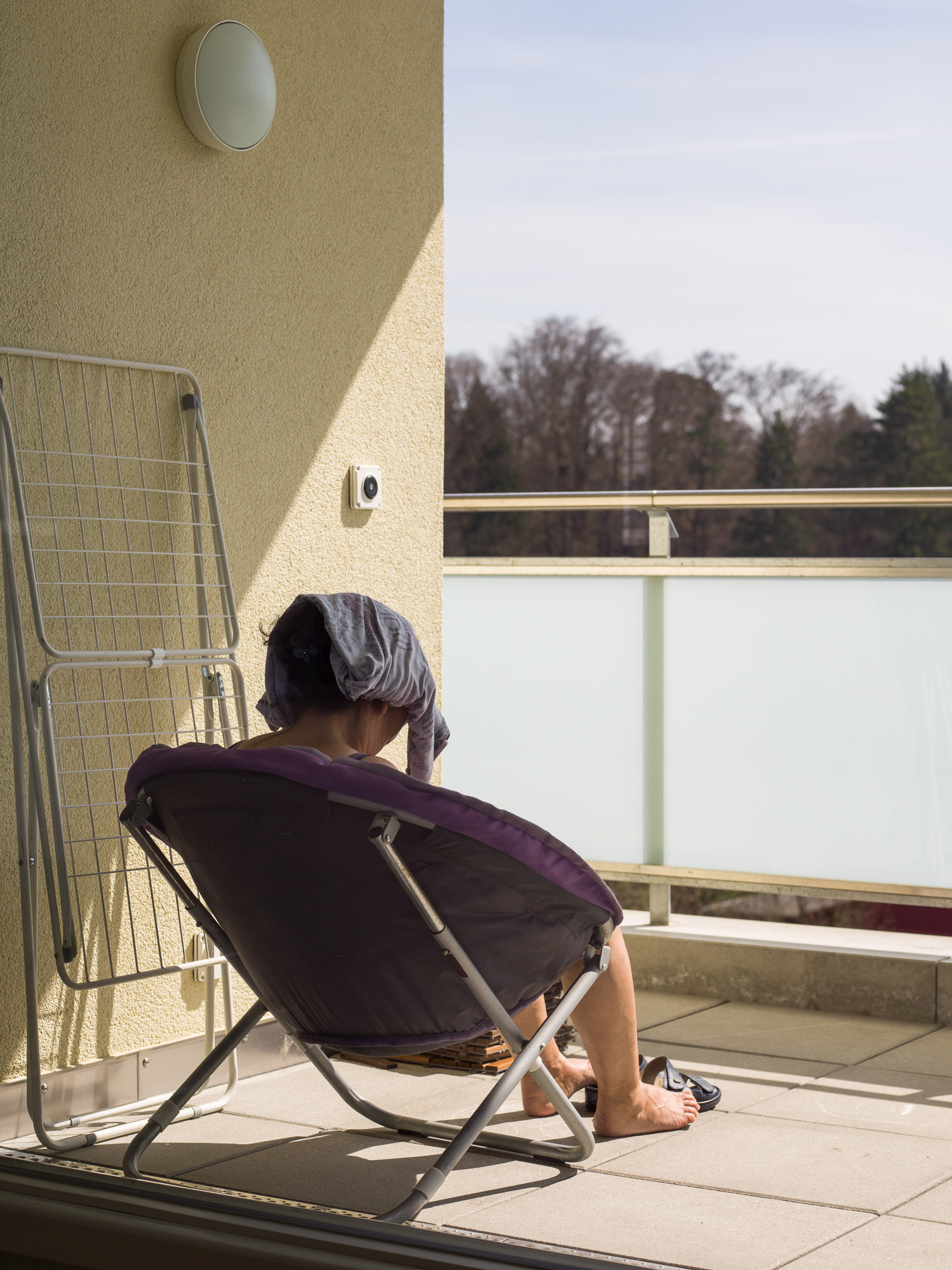 Fotografisches Storytelling und Reportage über den Besuch meiner Schwiegermutter aus der Mongolei, die sich auf dem Balkon an der Sonne entspannt.