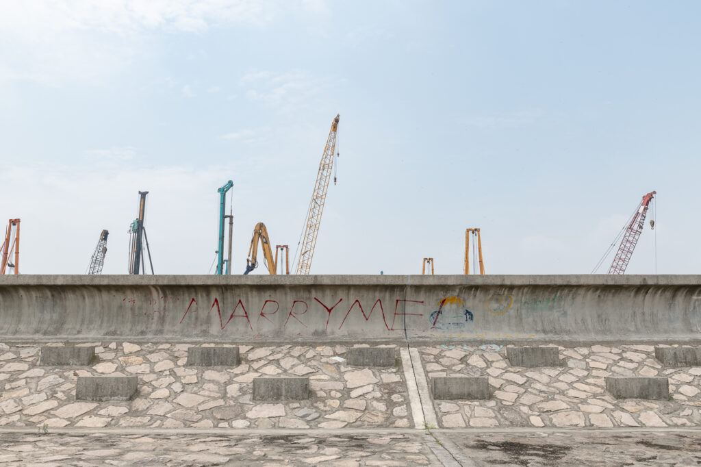 Reportage und Buchprojekt über den Huangpu River in Shanghai, China. Aufnahme einer Schutzmauer mit einem Frachthafen im Hintergrund.
