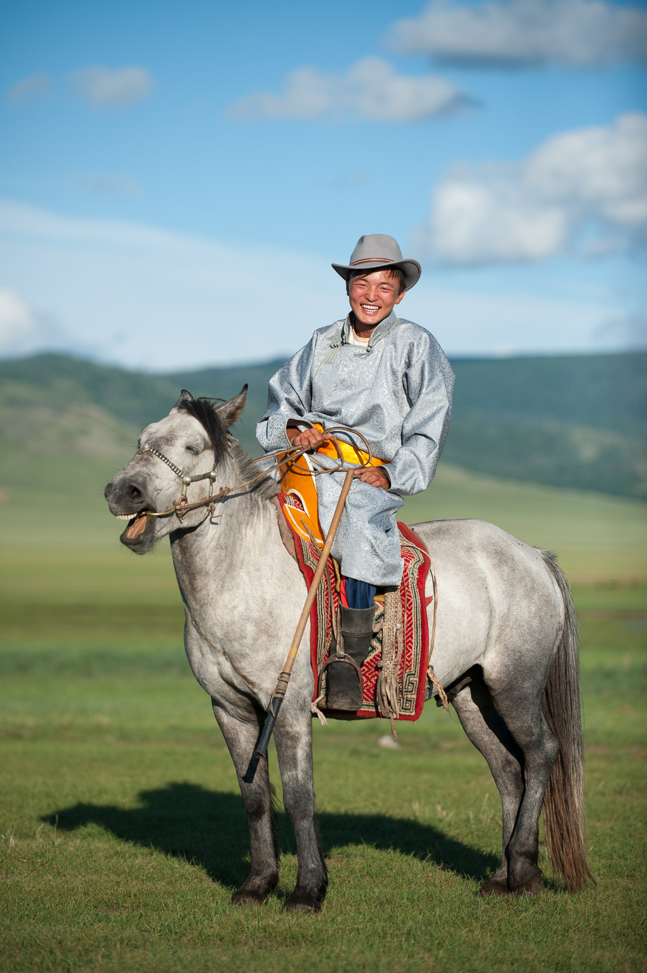 Portrait von einem Nomaden auf einem Pferd, die mongolische Steppe im Hintergrund. Reportage über die Nomaden in der Mongolei.