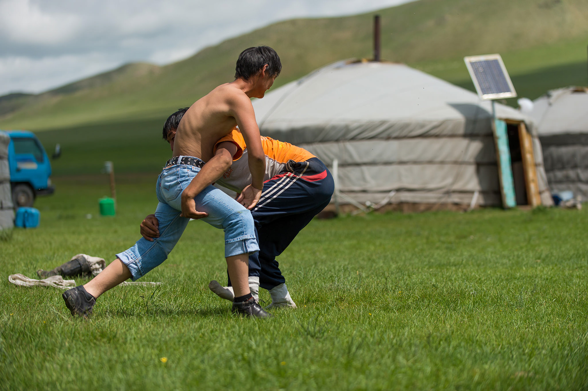 Fotoreportage über die Nomaden in der Mongolei. Aufnahme von zwei Männern beim Schwingen vor einer Jurte.